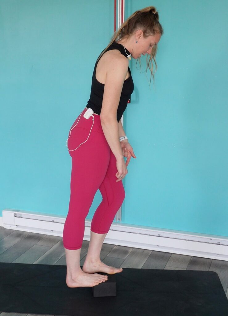 Dr. Chloe standing on a yoga block with her right heel dropped off the back stretching her right calf